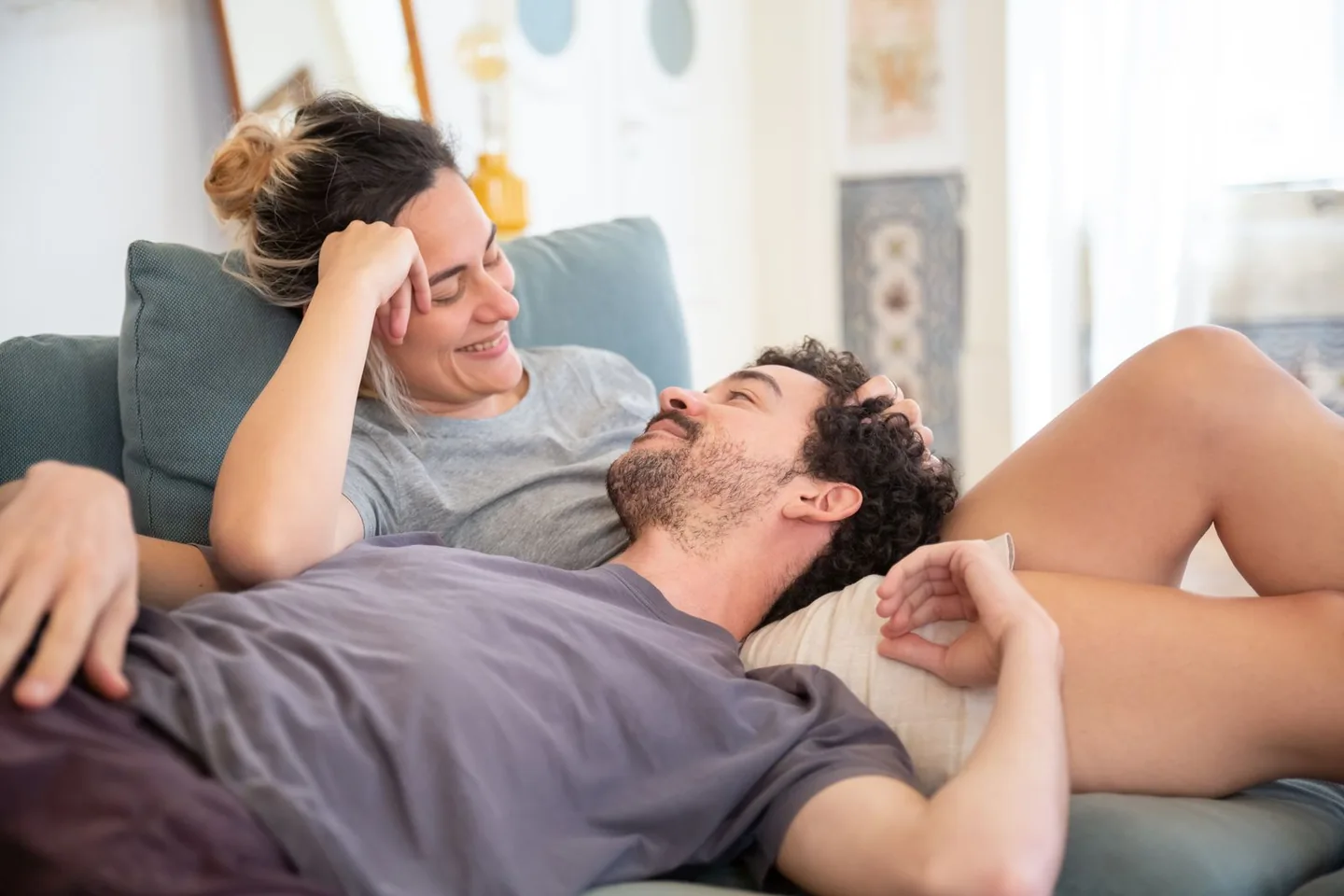 Una pareja adulta descansa en el sofá, él apoya la cabeza en el regazo de ella mientras sonríen